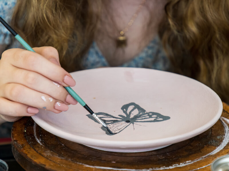 A woman decorates a plate with a butterfly in a pottery painting class.